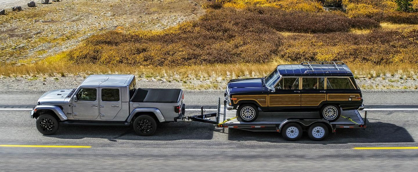 The 2021 Jeep Gladiator High Altitude towing a flatbed with a classic Jeep Grand Wagoneer on it.