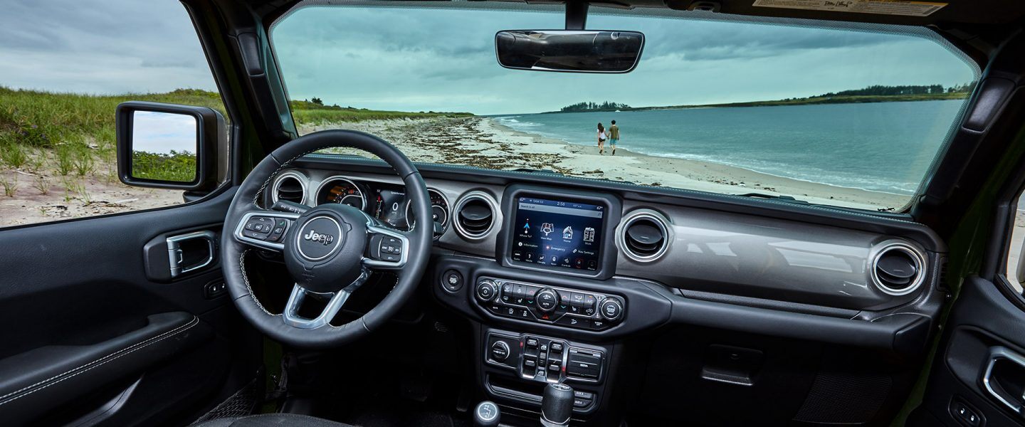 The interior of the 2021 Jeep Wrangler Sahara focusing on the steering wheel, entertainment center and dashboard.