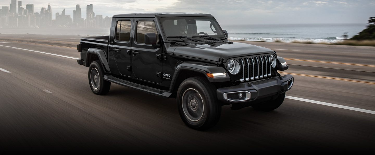 The 2022 Jeep Gladiator Overland being driven on an open road, a city skyline in the distance behind it.